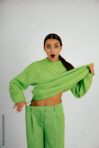 Vertical shocked dazed beauteous brunette woman with open mouth in big green costume present thin, slim sportive abdomen