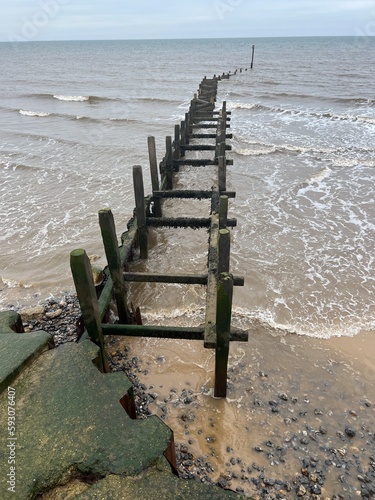 Wooden breakwater on the shore of the sandy beautiful beach at Overstrand Norfolk East Anglia scenic view out to horizon across ocean in cloudy weather. photo