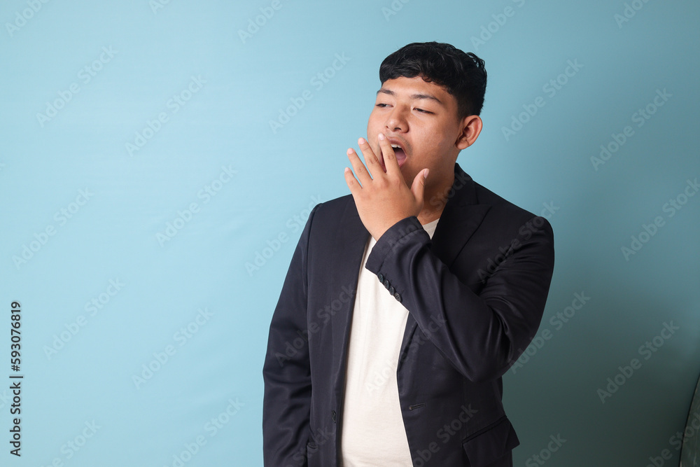 Portrait of young Asian business man in casual suit yawning in bored expressions. Isolated image on blue background Portrait of young Asian business man in casual suit yawning in bored expressions. Isolated image on blue background