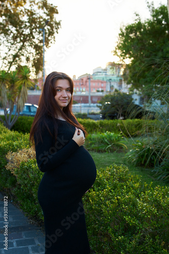 pregnant girl holding her belly, around flowers and plants, in garden
