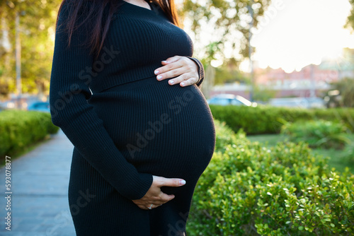 pregnant girl holding her belly, around flowers and plants, in garden