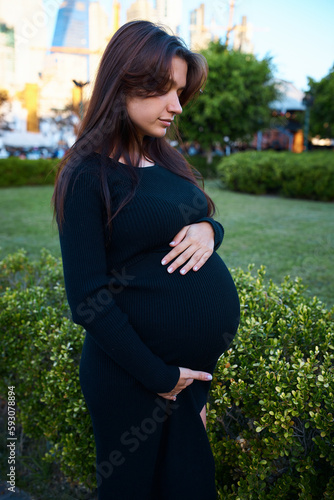 pregnant girl holding her belly, around flowers and plants, in garden