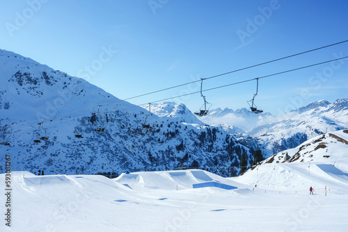 Ski lifts over snow covered landscape with mountains in background on sunny day, winter holiday travel concept