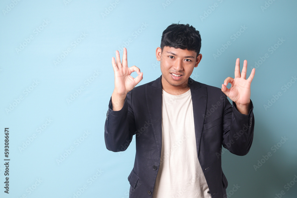 Portrait of young Asian business man in casual suit with happy expressions and double agree hand gestures. Isolated image on blue background Portrait of young Asian business man in casual suit with happy expressions and double agree hand gestures. Isolated image on blue background