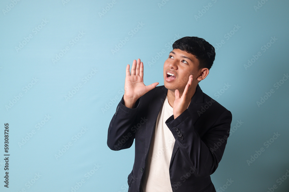 Portrait of young Asian business man in casual suit shouting to the distance. Isolated image on blue background Portrait of young Asian business man in casual suit shouting to the distance. Isolated image on blue background