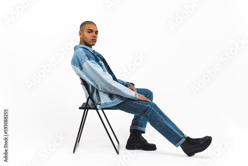 African American male model in full denim outfit sitting on a chair on white background . High quality photo