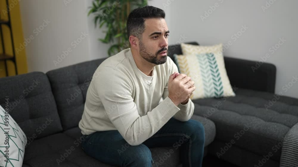 Young hispanic man sitting on sofa with worry expression at home Young hispanic man sitting on sofa with worry expression at home