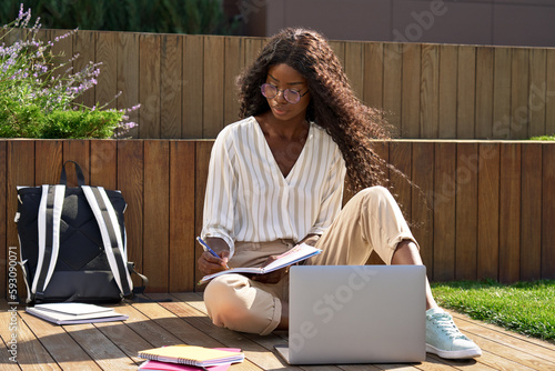 Obraz na plátne Young black African ethnic woman university student learning online using laptop computer having virtual education remote class training seminar studying outdoors sitting outside uni campus area
