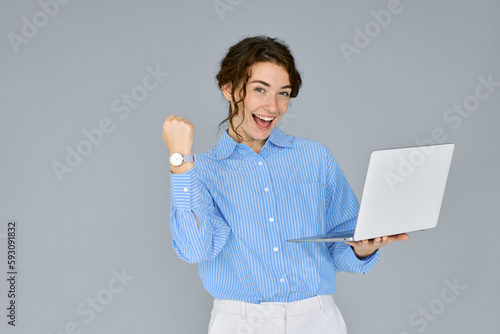 фотографія Young happy excited business woman executive holding laptop computer raising fist in yes gesture celebrating online win, business success, good result or reward standing isolated on grey background
