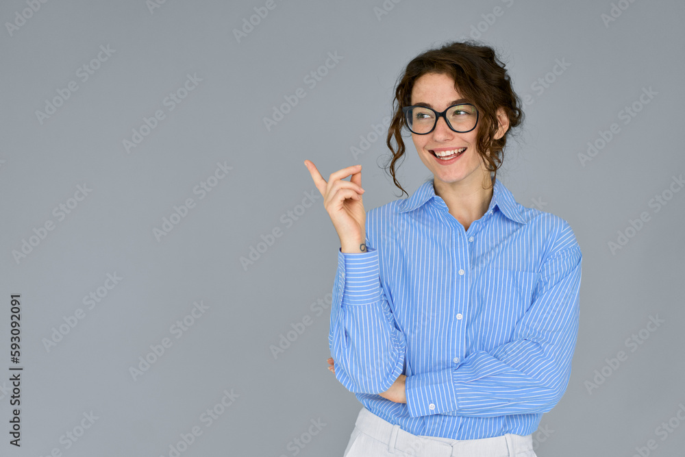 Happy young smiling professional business woman wearing blue shirt glasses looking away pointing finger at copy space showing aside presenting ads promotion standing isolated at gray background. Happy young smiling professional business woman wearing blue shirt glasses looking away pointing finger at copy space showing aside presenting ads promotion standing isolated at gray background.