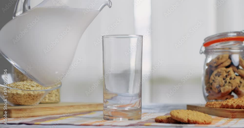 Pour fresh homemade milk from a jug into glass. Splash of pouring milk into a glass from a jug in a room table, cream flow pours fresh milk from jug into glass serving table for a homemade breakfast. Pour fresh homemade milk from a jug into glass. Splash of pouring milk into a glass from a jug in a room table, cream flow pours fresh milk from jug into glass serving table for a homemade breakfast.