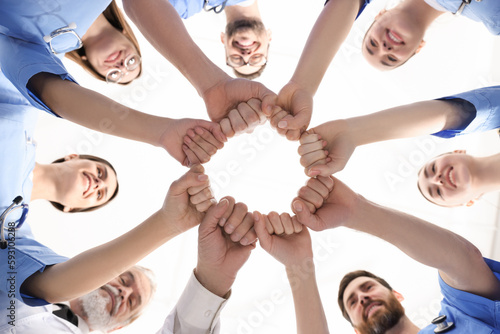 Doctor and interns holding fists together against white background, bottom view