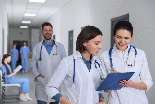 Smart medical students with clipboard in college hallway  space for text