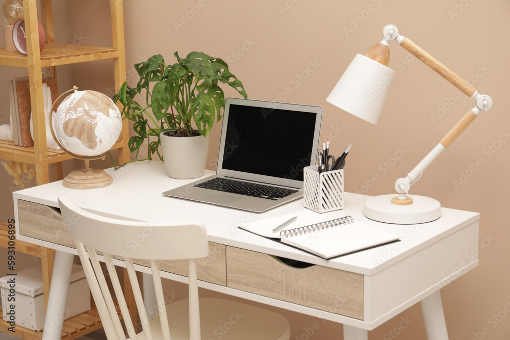 Cozy workplace with modern laptop on desk and comfortable chair at home Cozy workplace with modern laptop on desk and comfortable chair at home