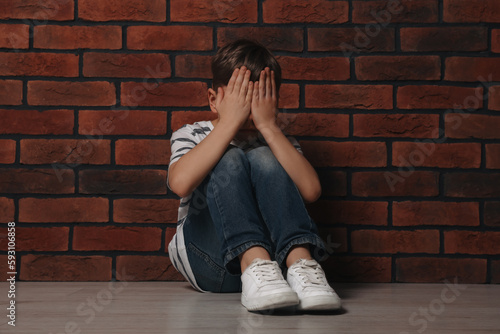 Upset boy sitting on floor near brick wall. Children's bullying