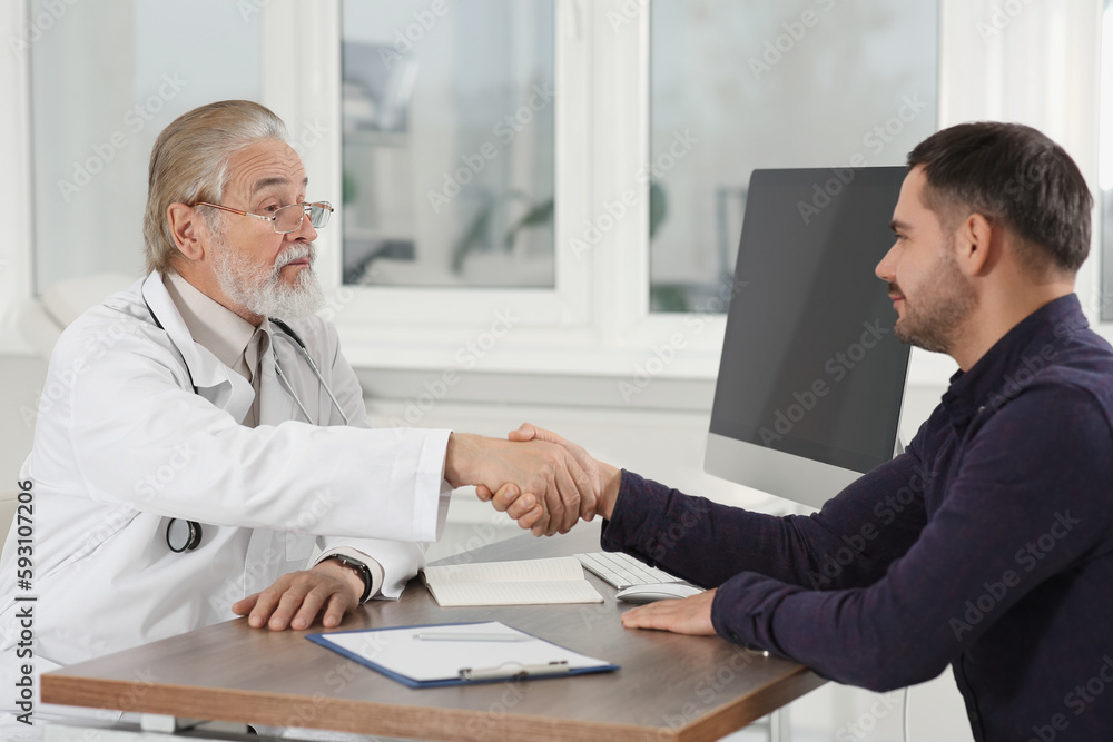 Senior doctor shaking hands with patient at wooden table in clinic Senior doctor shaking hands with patient at wooden table in clinic
