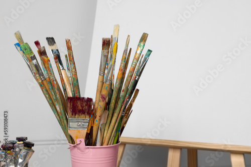 Easel with blank canvas and different art supplies near white wall. Space for text