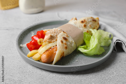 Delicious pita wrap with sausage, french fries and vegetables on light gray table