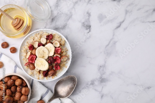 Delicious oatmeal with freeze dried berries, banana and hazelnuts served on white marble table, flat lay. Space for text photo