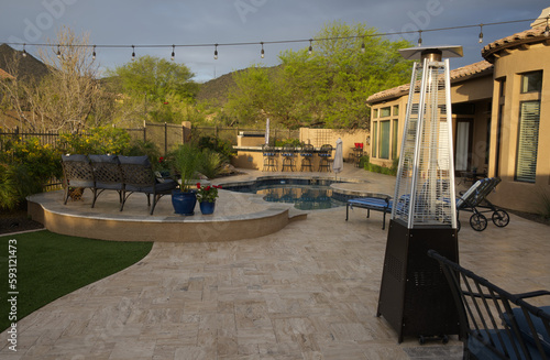 A desert landscaped backyard in Arizona featuring a travertine tiled pool deck with spa and outdoor kitchen.