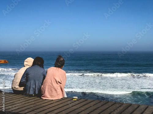 Sunny day bliss: three women enjoy a warm hug on a terrace overlooking the ocean