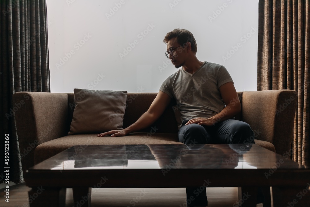 Fototapeta premium Lonely asian man sits on the sofa thinking of his lover.