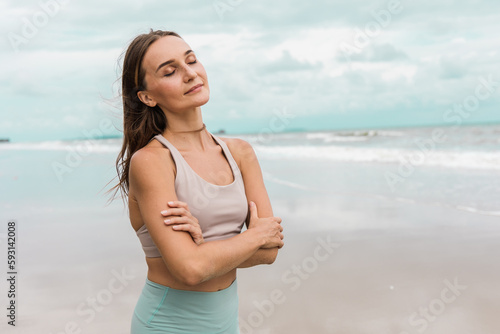 A fit woman standing on beach with her eyes closed, breathing deeply