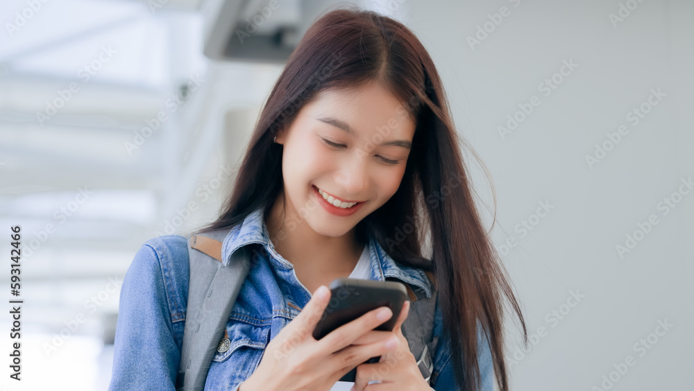 Young asian woman smiling using mobile smart phone outdoor. Happy female tourist wearing jeans jacket and holding smartphone at public Young asian woman smiling using mobile smart phone outdoor. Happy female tourist wearing jeans jacket and holding smartphone at public
