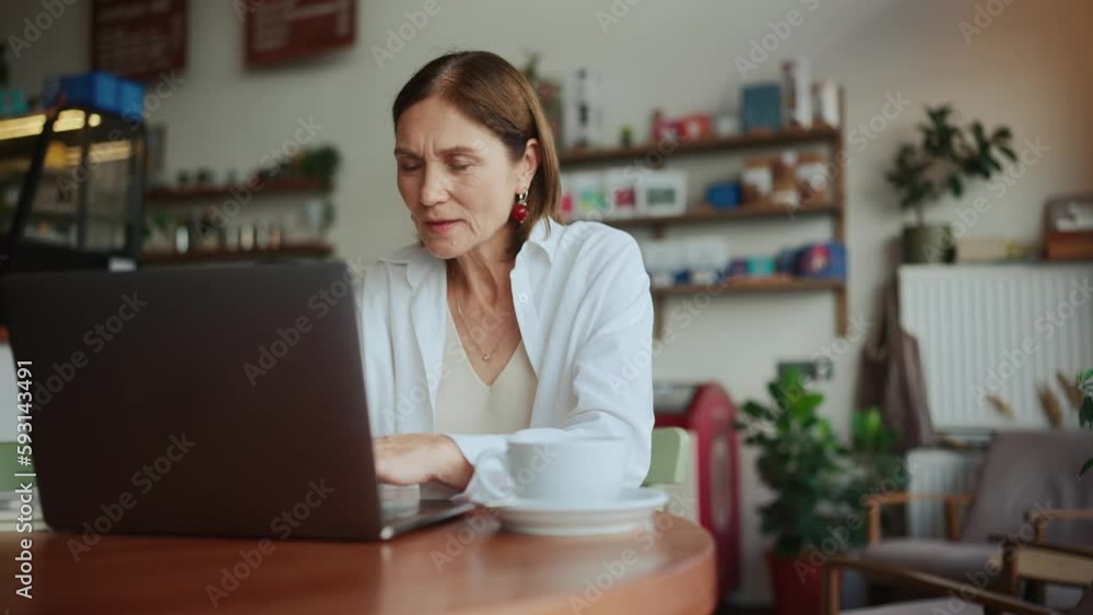 Concentrated elderly woman in white shirt working remotely on laptop in cafe Concentrated elderly woman in white shirt working remotely on laptop in cafe
