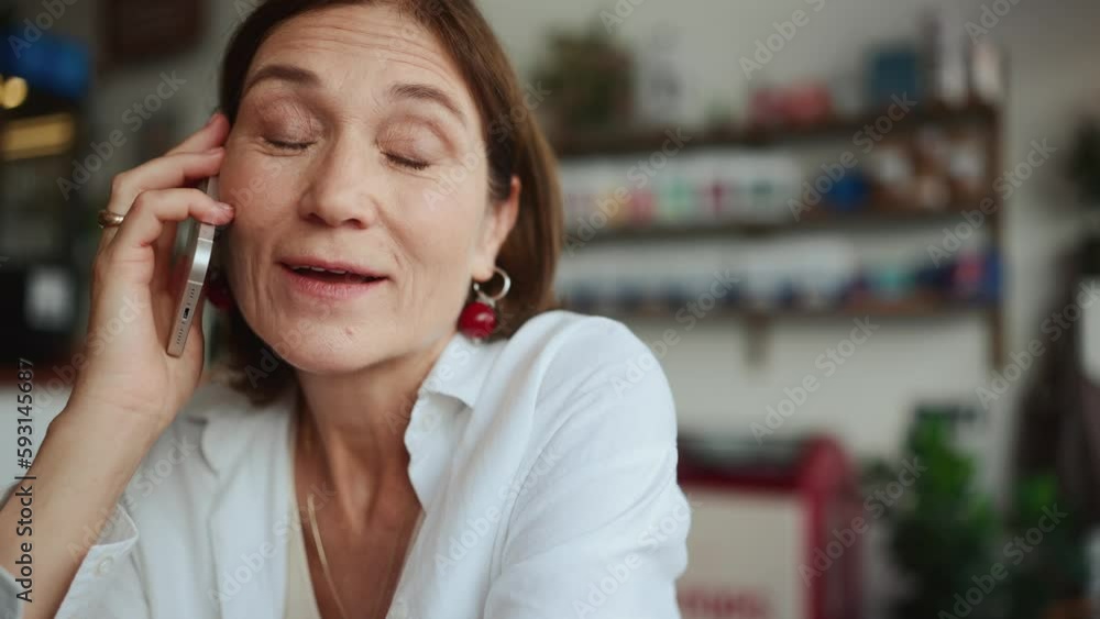 Smiling elderly woman in white shirt looking to side and talking on cell phone in cafe Smiling elderly woman in white shirt looking to side and talking on cell phone in cafe