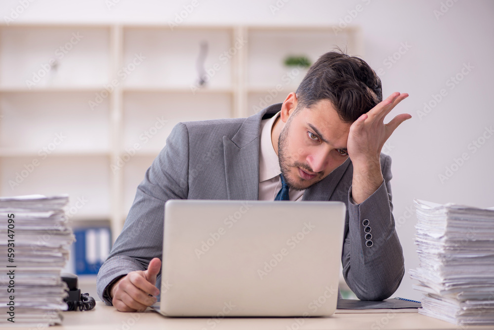 Young male employee unhappy with excessive work in the office Young male employee unhappy with excessive work in the office