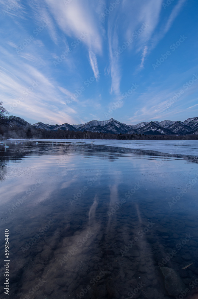 雲の流れる青空を湖面に反射する冬の湖。北海道の屈斜路湖。