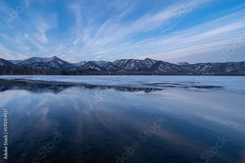 雲の流れる青空を湖面に反射する冬の湖。北海道の屈斜路湖。