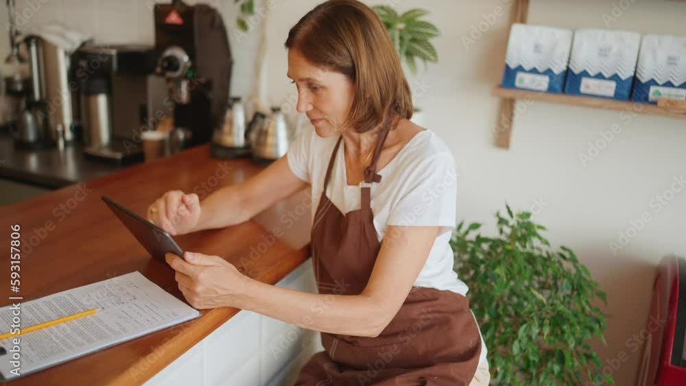 Confident mature woman barista texting on digital tablet in cafe Confident mature woman barista texting on digital tablet in cafe