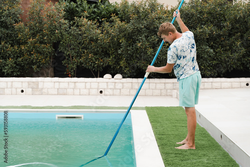 Man brushing a dirty outdoor swimming pool with vacuum cleaner
