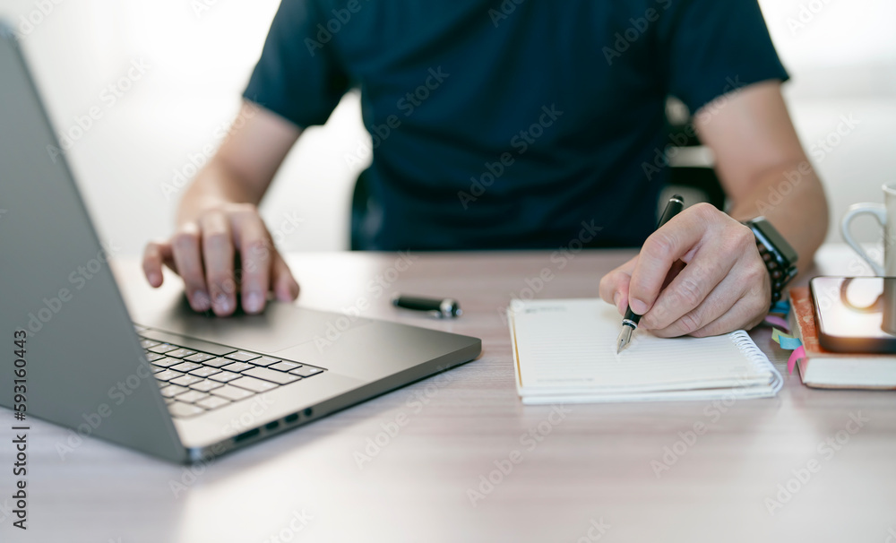 Young man writing down on notebook and using laptop computer, sitting at home office. Young man writing down on notebook and using laptop computer, sitting at home office.