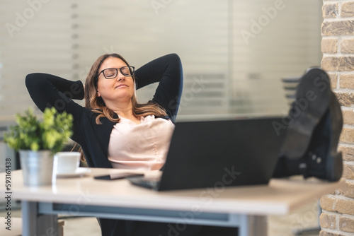 Confident manager leaning on chair with legs up on desk in office and thinking about something beautiful