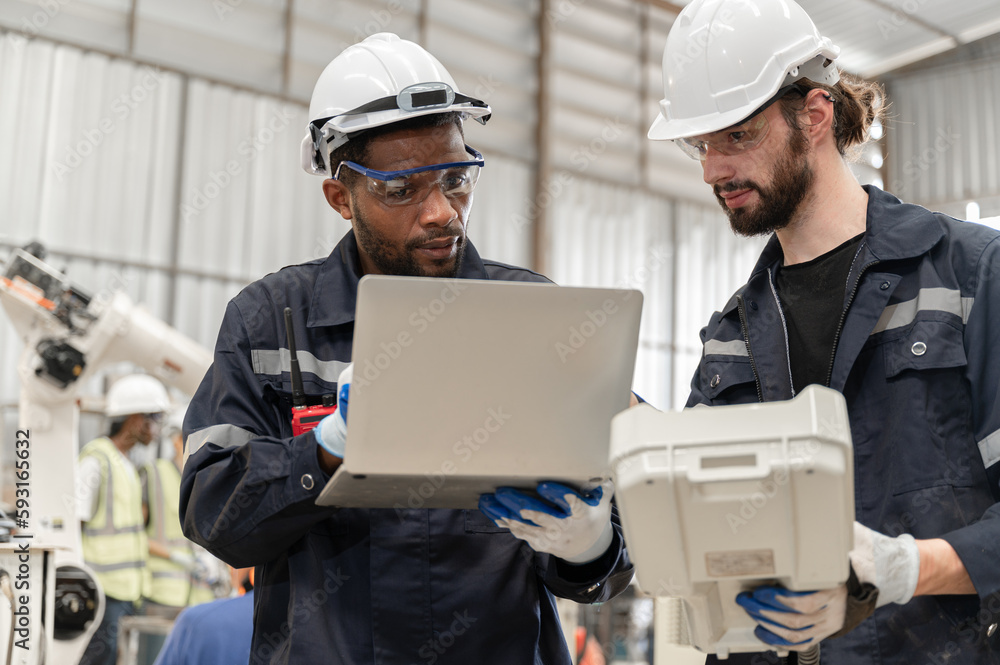 Caucasian and African American technician engineer man use remote control and computer notebook with checking machine arm robot at factory Caucasian and African American technician engineer man use remote control and computer notebook with checking machine arm robot at factory