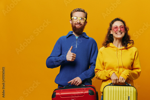 Woman and man smiling, suitcases in hand with yellow and red suitcase smiling merrily and crooked, yellow background, going on a trip, family vacation trip, newlyweds.