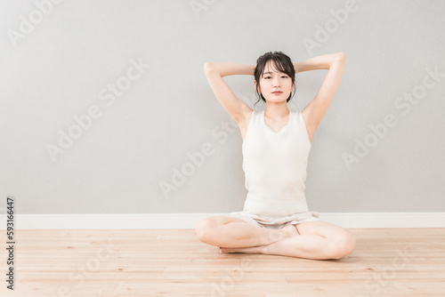 フローリングに座って考えごとをするアンニュイ表情のアジア人女性（脱毛・美容） 
