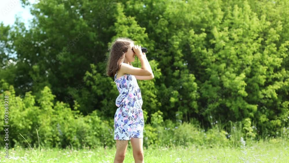 Cute teenage girl looks through binoculars and waves her hand in a summer park Cute teenage girl looks through binoculars and waves her hand in a summer park