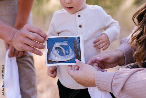 Parents holding ultrasound photo of twins with their son photo