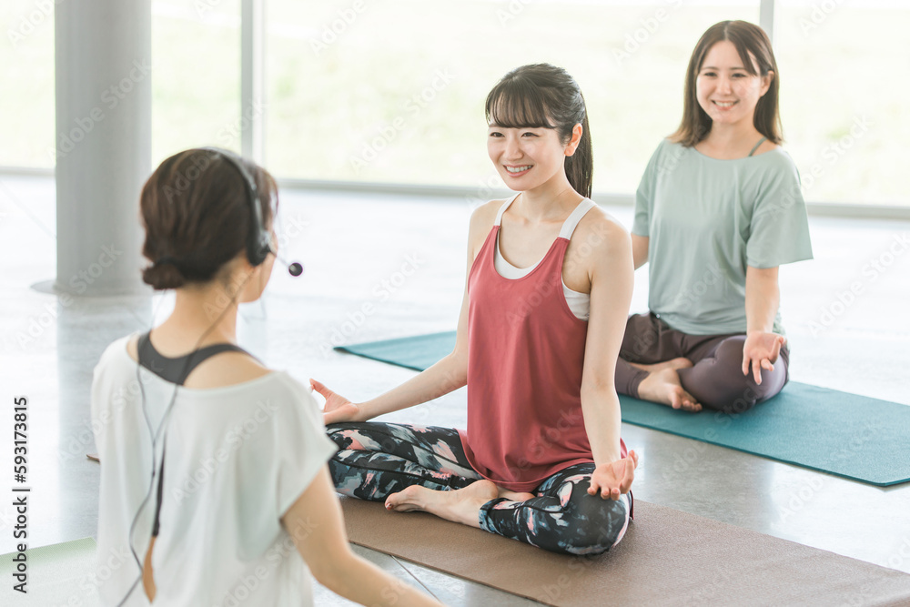 Obraz premium マイクをつけたヨガ講師とヨガ教室・ピラティスでヨガを習う女性達 