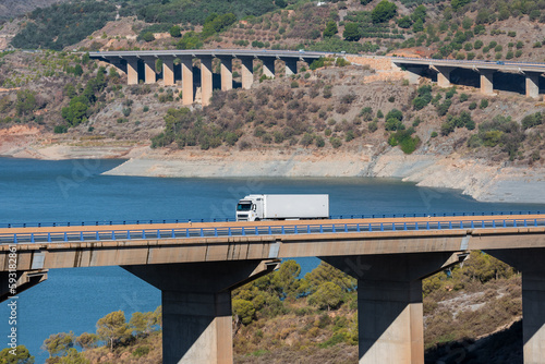 Truck with a refrigerated semi-trailer driving through a viaduct over a swamp  in the background several more viaducts.