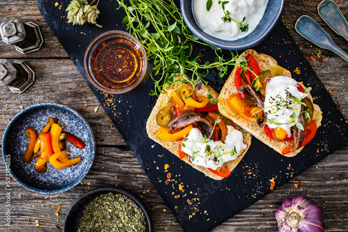 Tasty sandwiches - toasted bread with burrata cheese, anchovies, bell pepper, olives, tomatoes and thyme on wooden table
 photo