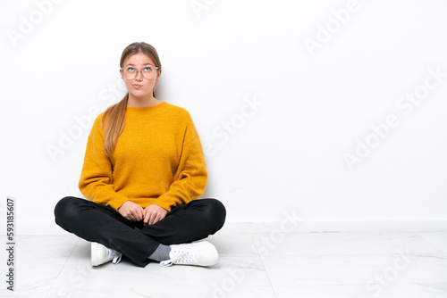 Young caucasian woman sitting on the floor isolated on white background and looking up © luismolinero