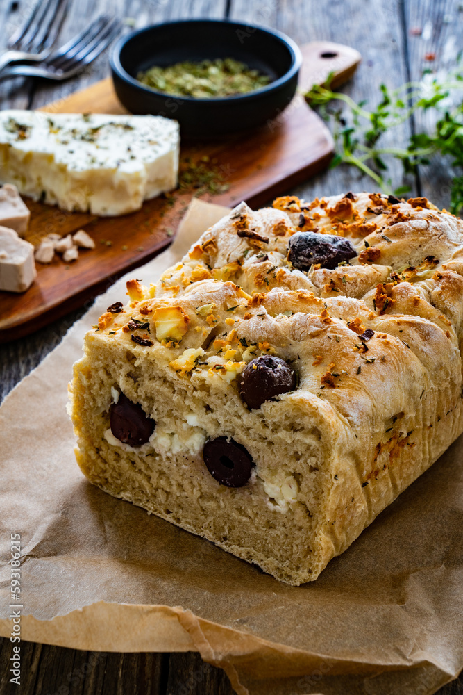 Loaf of village, fresh bread with feta and black olives on wooden table
