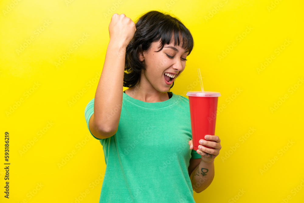 Young Argentinian woman holding a soda isolated on yellow background celebrating a victory Young Argentinian woman holding a soda isolated on yellow background celebrating a victory