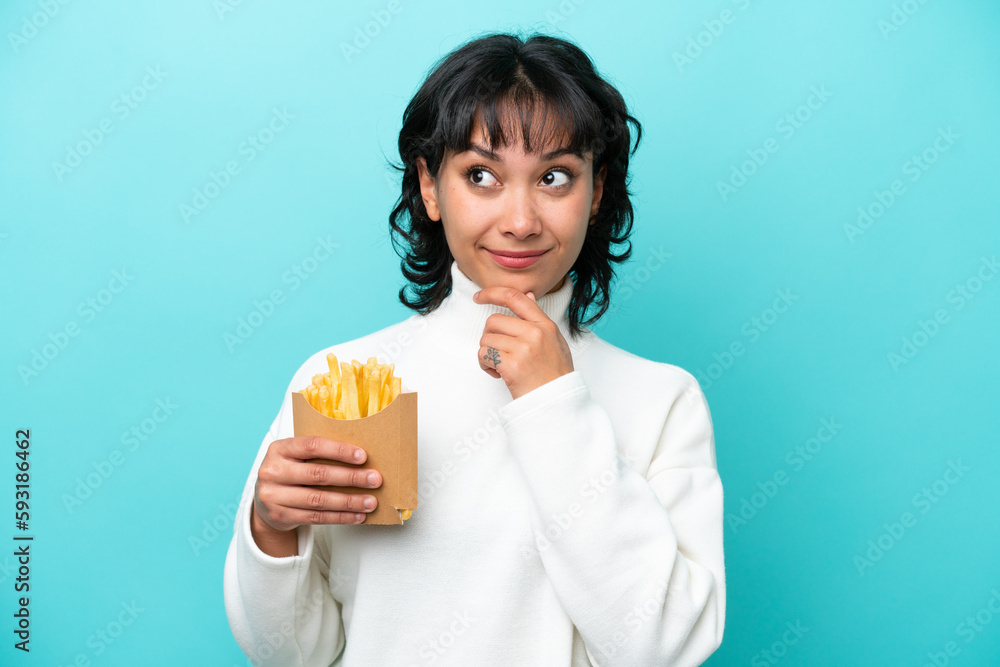 Young Argentinian woman holding fried chips isolated on blue background looking up while smiling Young Argentinian woman holding fried chips isolated on blue background looking up while smiling