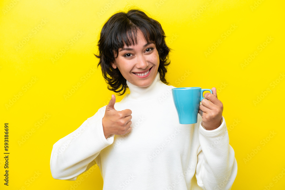 Young Argentinian woman holding cup of coffee isolated on yellow background with thumbs up because something good has happened Young Argentinian woman holding cup of coffee isolated on yellow background with thumbs up because something good has happened